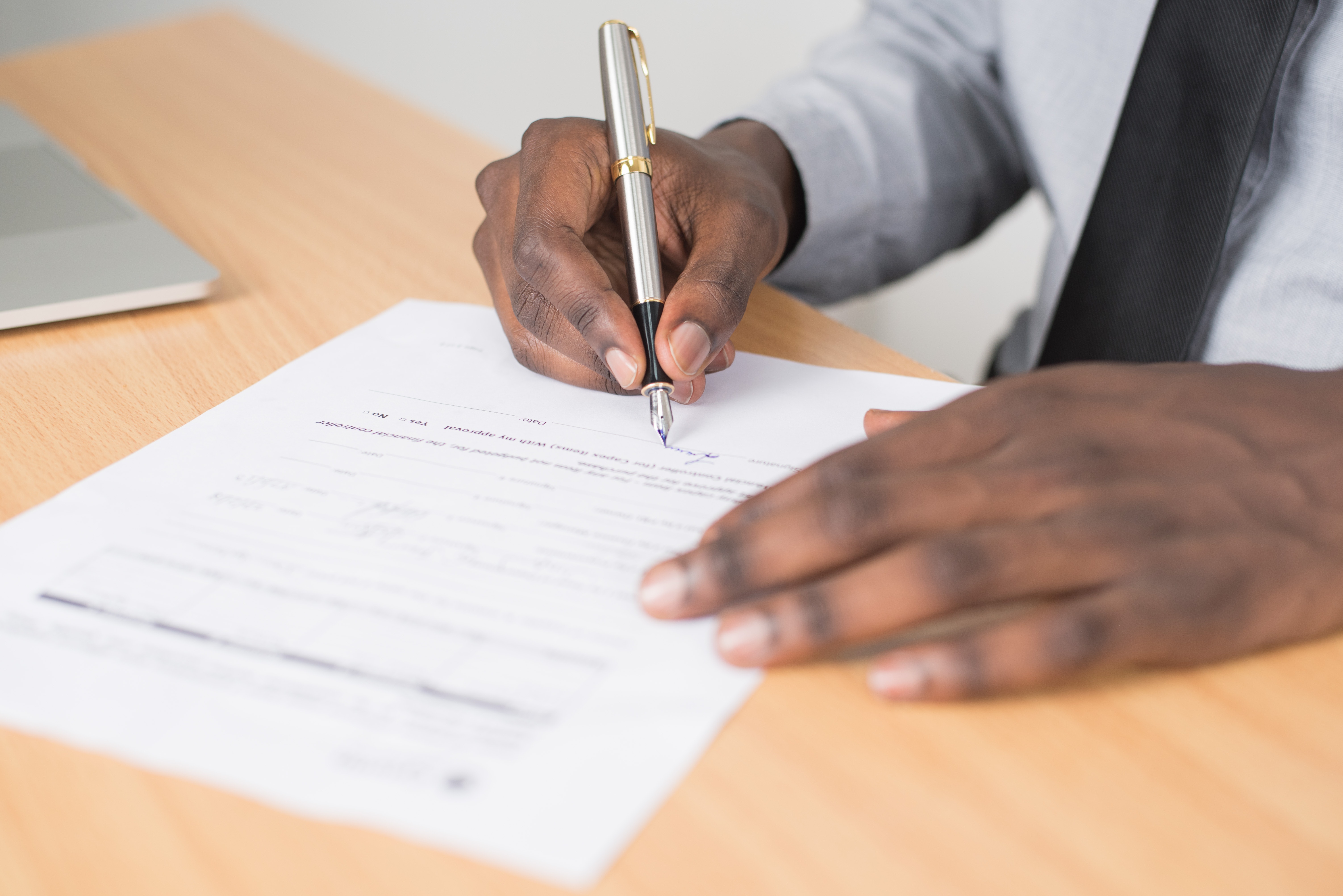 A car seller sits at a desk, signing car paperwork.