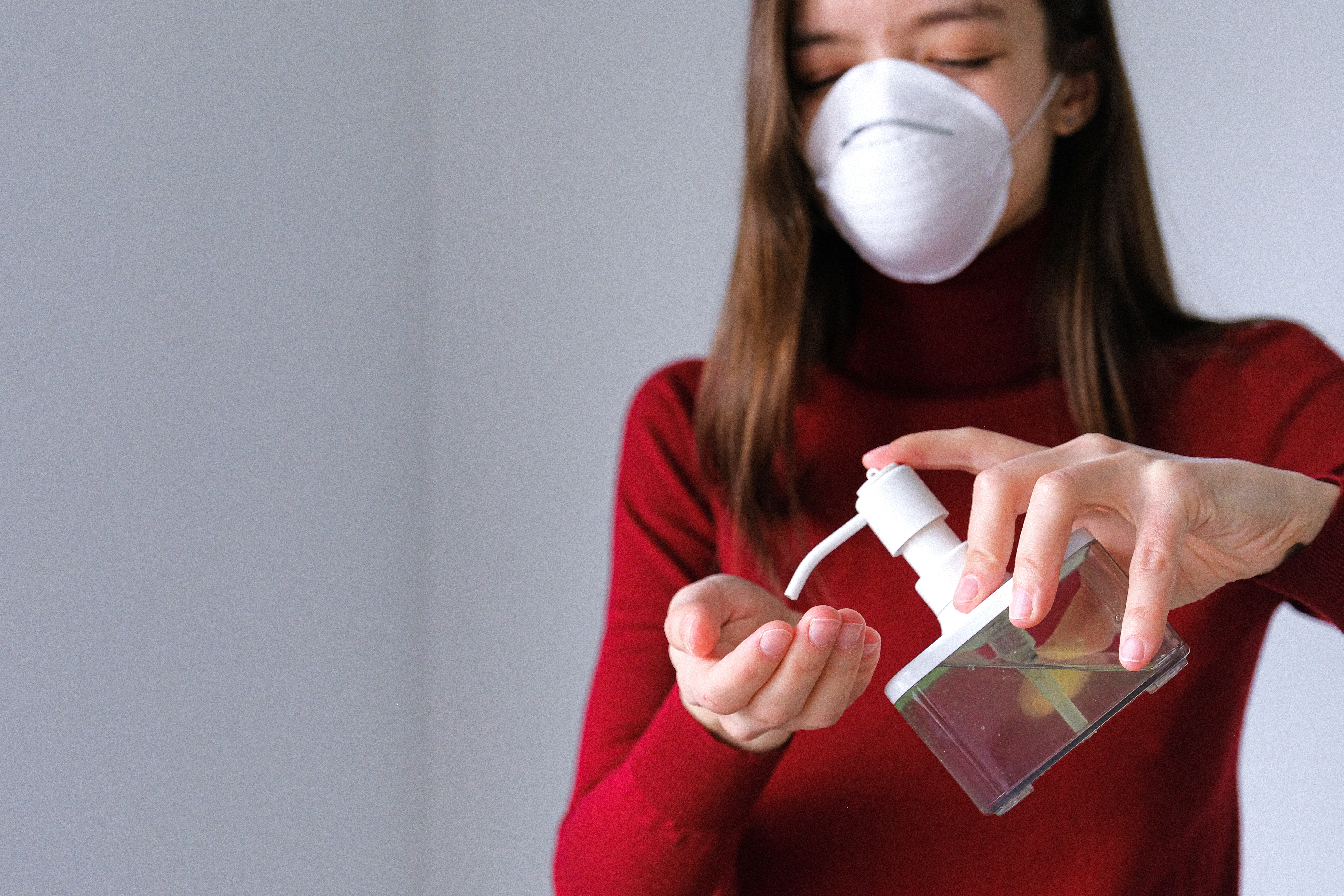 A person wearing a medical mask holds a bottle of hand sanitizer and squirts into their palm.