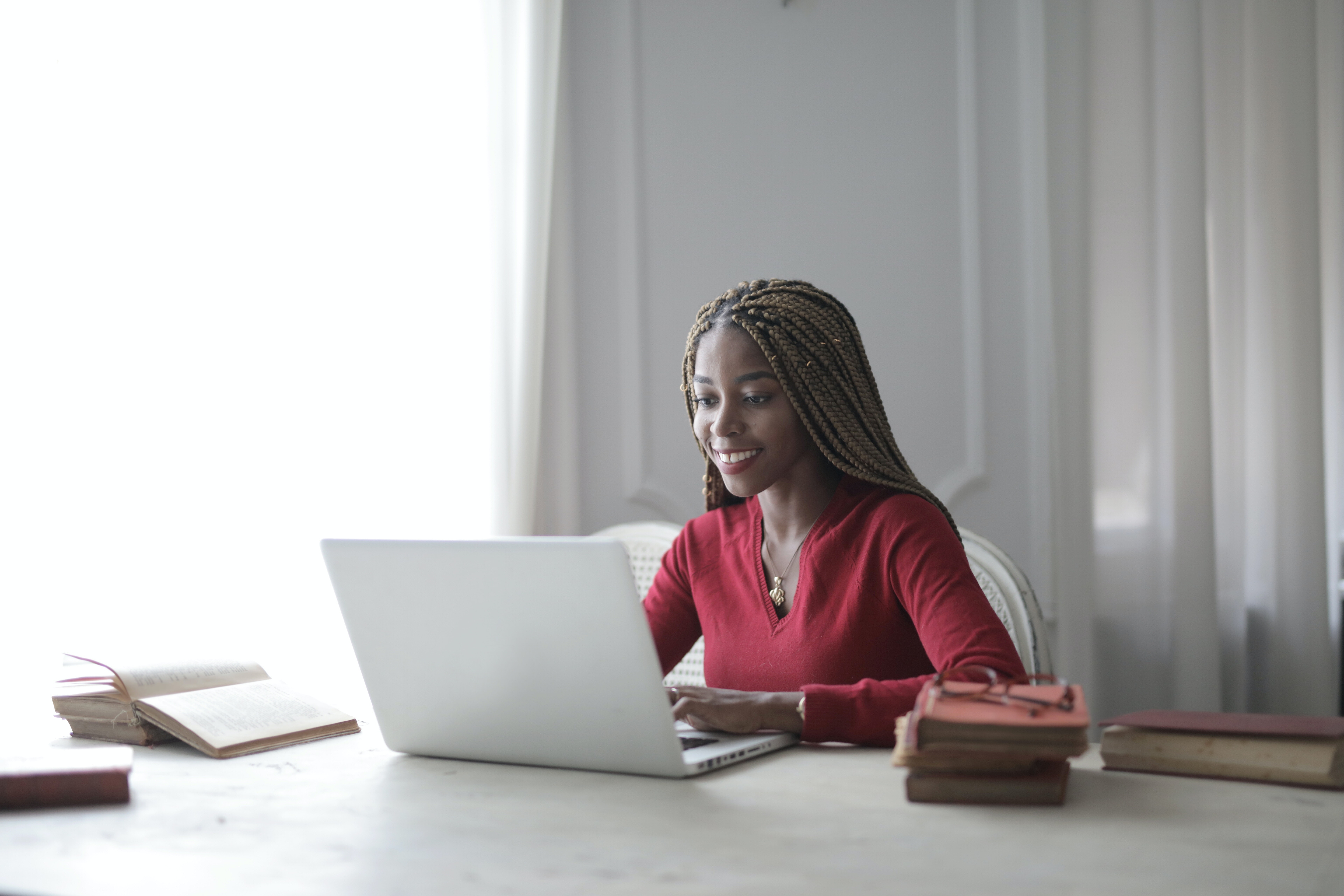 A smiling person sits at a desk and uses a laptop.